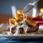 Steak and calamari with garlic cream sauce, served on a white plate with crispy golden rings stacked on top